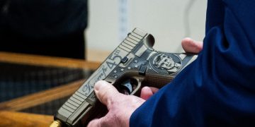 A closeup of former President Donald Trump's hands holding a Glock handgun his likeness on it.