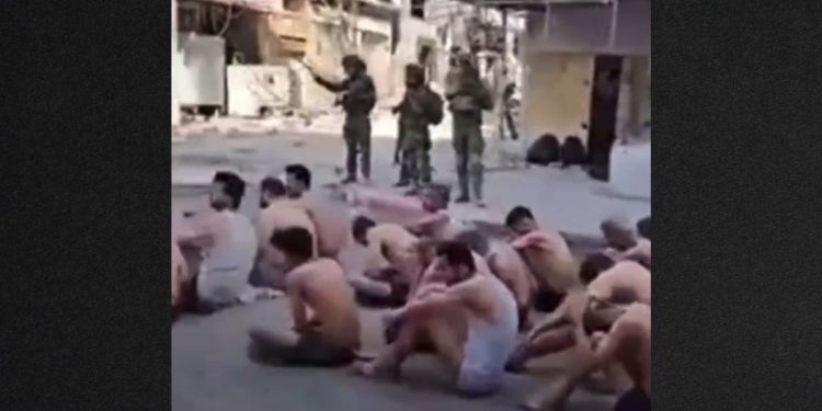Prisoners sat on the street, stripped to their underwear, as they waited to be loaded onto truck.